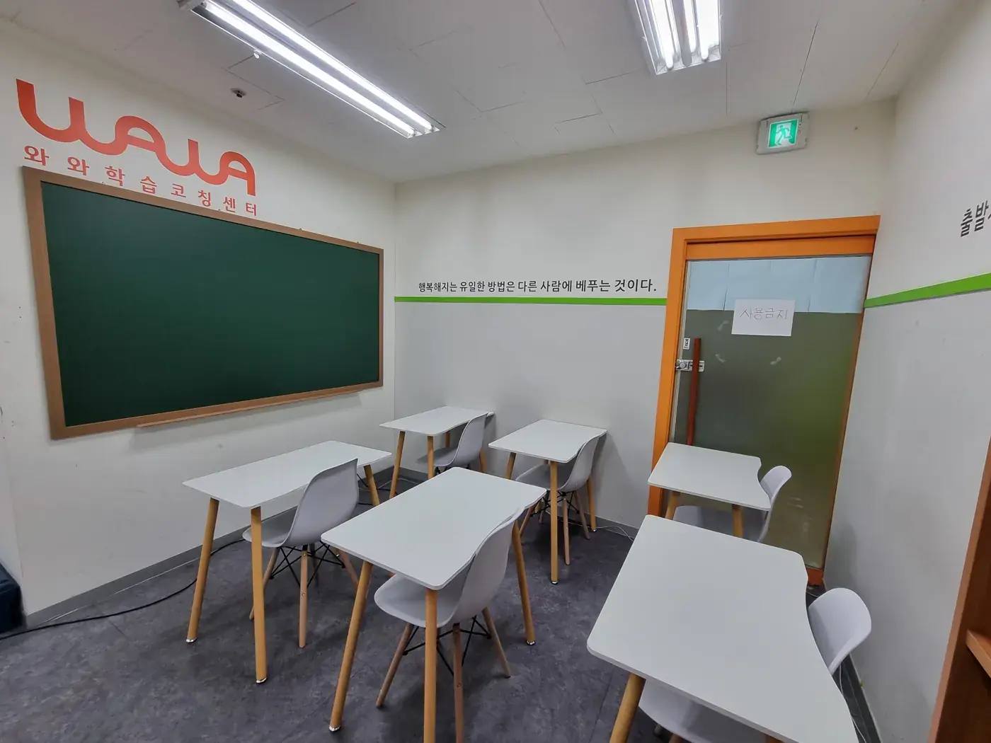 초록 칠판과 흰 책상, 흰 의자가 놓인 주황 문틀의 부평점 소규모 교실
